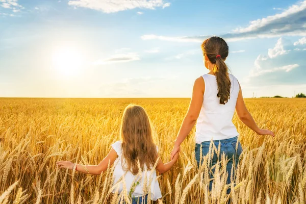 Mujer joven y su hija caminando en el campo de trigo dorado en el día soleado . — Foto de Stock