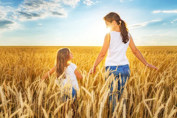 Mujer joven y su hija caminando en el campo de trigo dorado en el día soleado . — Foto de Stock
