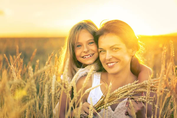 Giovane donna e sua figlia sul campo di grano dorato alla sera di sole . — Foto Stock