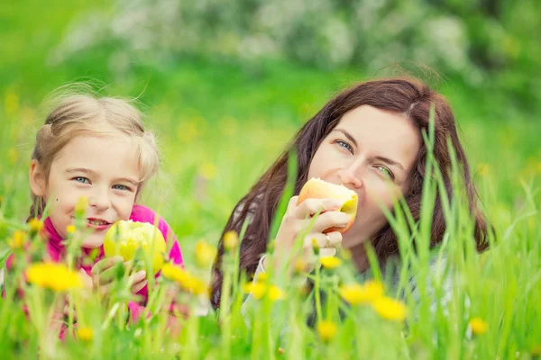 Anne ve kızı yeme elma yeşil yaz çayır üzerinde — Stok fotoğraf