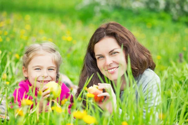 Anne ve kızı yeme elma yeşil yaz çayır üzerinde — Stok fotoğraf