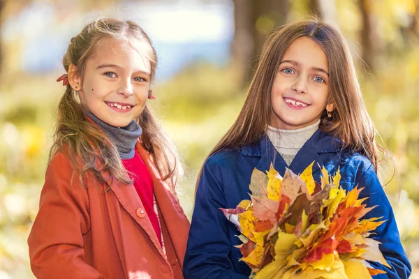 Zwei süße lächelnde 8-jährige Mädchen posieren zusammen in einem Park an einem sonnigen Herbsttag. — Stockfoto