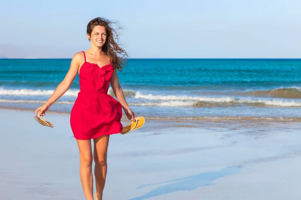 Kırmızı elbiseli genç kadın sahilde eğleniyor. — Stok fotoğraf