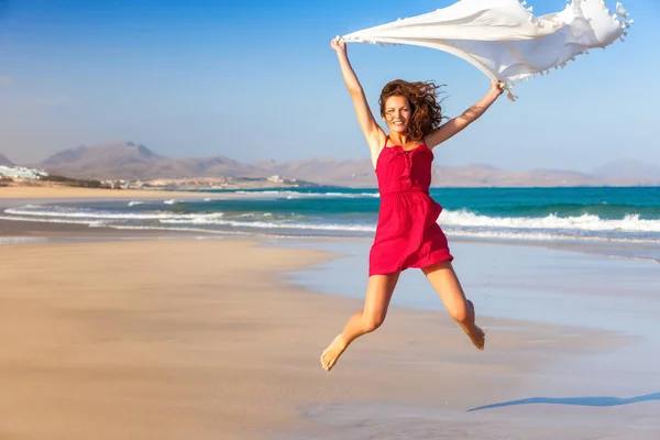 Jonge vrouw in rode jurk springen op het strand — Stockfoto
