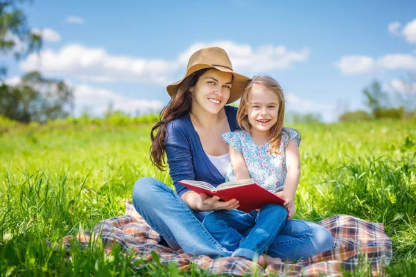 Moeder en dochter lezen boek over groene zomerweide — Stockfoto