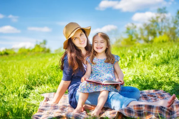Madre e hija leyendo libro sobre prado de verano verde — Foto de Stock