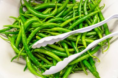 Yeşil biber maşa ile bir tabak içinde bir sürü 