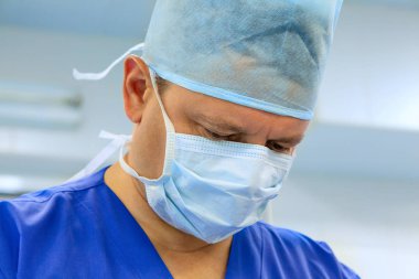 Close-up of male surgeon wearing surgical mask and cap performin