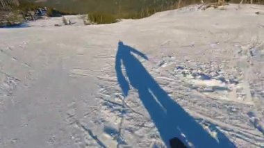 Güneşli bir günde bakımlı bir pistte yarışan bir kayakçının birinci şahıs görüntüsü. Uzun gölgeler parlak kar üzerinde süzülür, hızlı oyma dönüşleri ve alp manzarası. Saf kış tatili ve...