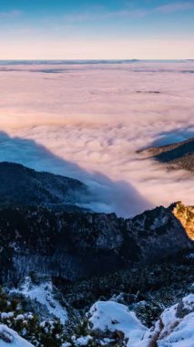 Gün doğumunda karlı bir dağ vadisinde sürüklenen sisli bulutlar. Sabahları bulutların üzerinde huzurlu bir kış manzarası. Dikey olarak yüksek bir alp zirvesinden panoramik görüntüler
