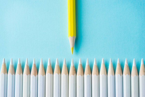 Business concept - lot of white pencils and color pencil on blue paper background. It's symbol of fight, leadership and communication.