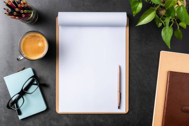 Siyah arka plan üzerinde spiral defter, saksı bitki, gözlük, kahve, kalem ve çanta ile kopya alanı.