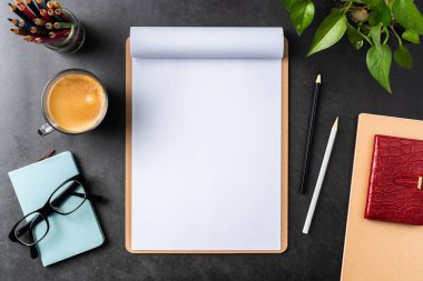 Siyah arka plan üzerinde spiral defter, saksı bitki, gözlük, kahve, kalem ve çanta ile kopya alanı.