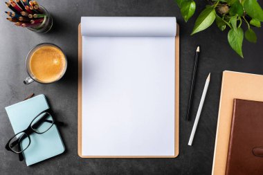 Siyah arka plan üzerinde spiral defter, saksı bitki, gözlük, kahve, kalem ve çanta ile kopya alanı.