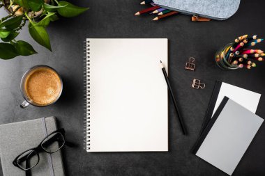 Siyah arka plan üzerinde spiral defter, saksı bitki, gözlük, kahve, kalem ve çanta ile kopya alanı.