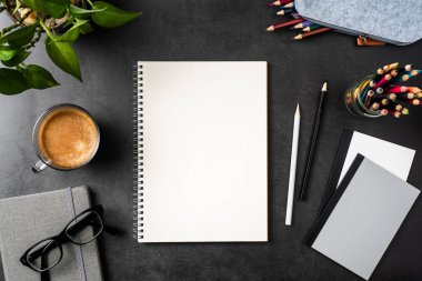 Siyah arka plan üzerinde spiral defter, saksı bitki, gözlük, kahve, kalem ve çanta ile kopya alanı.