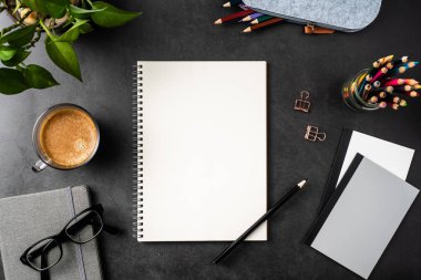 Siyah arka plan üzerinde spiral defter, saksı bitki, gözlük, kahve, kalem ve çanta ile kopya alanı.
