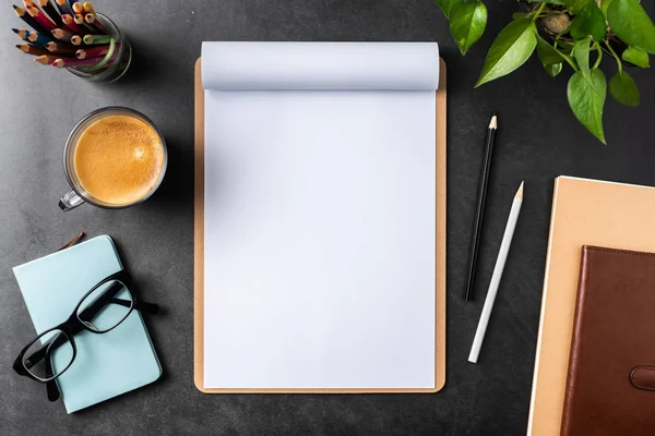 Siyah arka plan üzerinde spiral defter, saksı bitki, gözlük, kahve, kalem ve çanta ile kopya alanı.