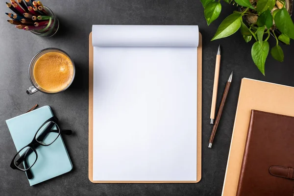 Siyah arka plan üzerinde spiral defter, saksı bitki, gözlük, kahve, kalem ve çanta ile kopya alanı.