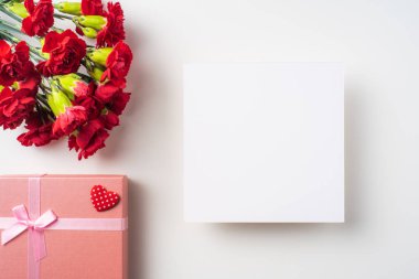 Beyaz arka planda izole kırmızı karanfil, tebrik kartı ve hediye kutusu bir demet üst görünümü.