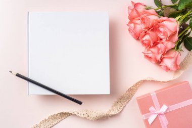 Pembe gül buketi, hediye kutusu, defter, kalem ve pembe arka plan üzerinde vintage kurdele