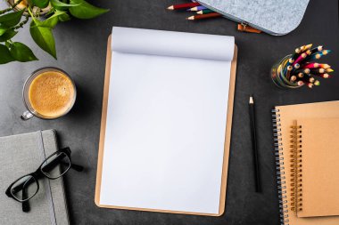 A4 kağıdı, saksı bitkisi, bardak, kahve, kalem ve siyah arkaplan üzerine not defterleri olan işyeri.