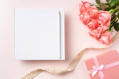 Pembe gül buketi, hediye kutusu, defter, kalem ve pembe arka plan üzerinde vintage kurdele