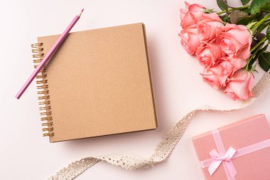 Pembe gül buketi, hediye kutusu, beyaz defter, kalem ve pembe arka plan üzerinde vintage kurdele