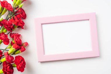 Beyaz arka plan üzerinde izole kırmızı karanfil ve fotoğraf çerçevesi demet üst görünümü