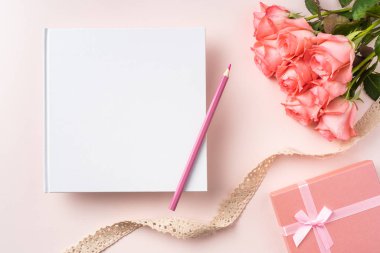 Pembe gül buketi, hediye kutusu, beyaz defter, kalem ve pembe arka plan üzerinde vintage kurdele