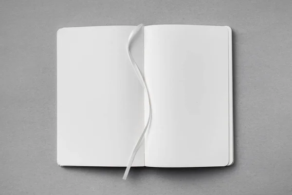 モックアップのための灰色の背景にリボンブックマーク付き開いた白いノートブックのトップビュー — ストック写真