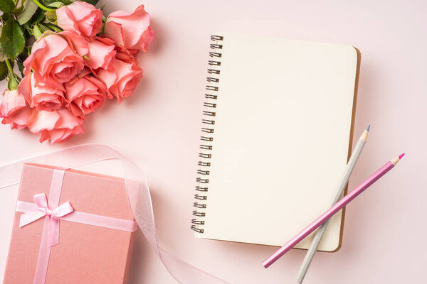 Куча розовых роз, подарочная коробка, блокнот с карандашами и винтажной лентой на розовом фоне
.
