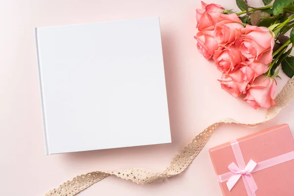 Bouquet of pink roses, gift box, notebook and vintage ribbon on pink background