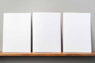 Kitapçıkta ve gri duvarda sahte bir duvarda duran 3 A4 derginin ön görünümü