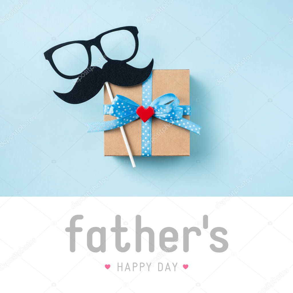 Top view of fathers day layout with gift box, silhouette of eyeglasses, mustache and lettering on blue background.