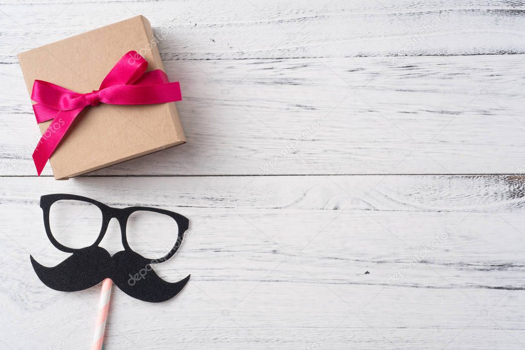 Fathers day layout with kraft pink ribbon gift box, eyeglasses and mustache on white wooden background