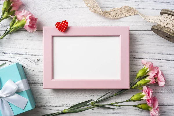 Anne gün mockup için beyaz Vintage ahşap arka planda fotoğraf çerçevesi, hediye kutusu, dantel şerit ve kalp ile pembe karanfil