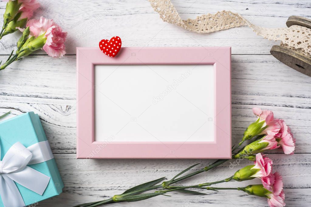 Pink carnations with photo frame, gift box, lace ribbon and heart on white vintage wooden background for mother day mockup