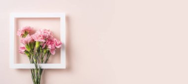 Pembe arka planda beyaz kare çerçeveli karanfil çiçek bileşimi