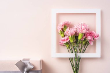 Pembe arka planda beyaz kare çerçeve ve hediye kutusu ile karanfil buket