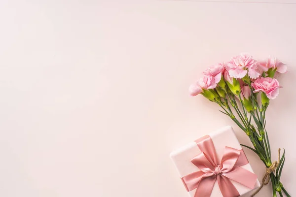 Karanfil demet, pembe arka planda hediye kutusu.