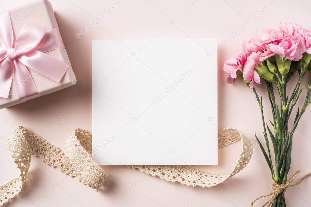 Top view of carnations, vintage lace ribbon, gift box and greeting card on pink background for mother day mockup