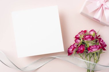 Kırmızı gül demet, boş beyaz kart, hediye kutusu ve pembe arka planda şerit