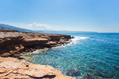 Uçurum. Akdeniz 'de bir adanın kayalık sahili. Dalgalar kayalara çarpar. Mavi gökyüzü ve deniz.