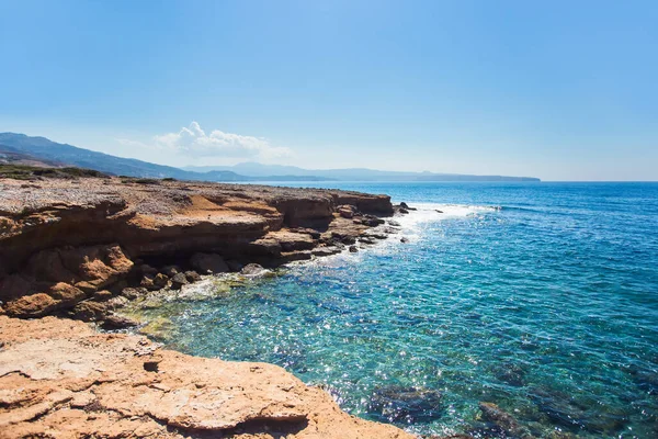 Uçurum. Akdeniz 'de bir adanın kayalık sahili. Dalgalar kayalara çarpar. Mavi gökyüzü ve deniz.