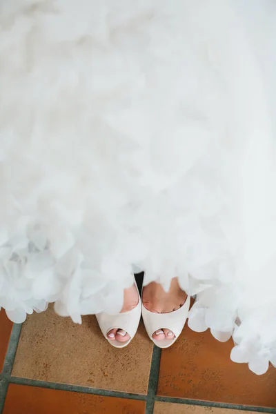 Beautiful bridal shoes with an open toe peek out from under wedding dress.