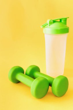 Sarı arka planda su için bir çift yeşil dambıl ve şişe. Sağlıklı yaşam tarzı, fitness konsepti. Seçici odak.