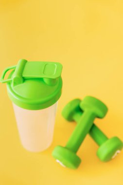 Sarı arka planda su için bir çift yeşil dambıl ve şişe. Sağlıklı yaşam tarzı, fitness konsepti. Seçici odak.