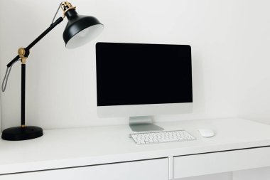 Siyah monitörü ve masa lambası olan beyaz bir masaüstü. İş yeri konsepti. Klavyeli boş bilgisayar ekranı. İç mekanda minimalizm. Öğrenci masaüstü.