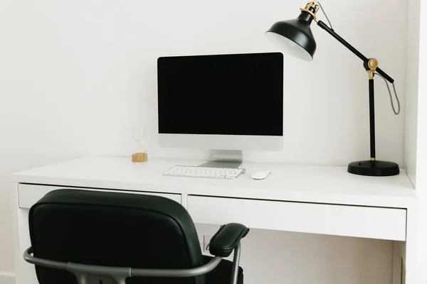 White work desk with black monitor, desk lamp and chair. Workplace concept. Minimalism in the interior. Work from home, student workplace.